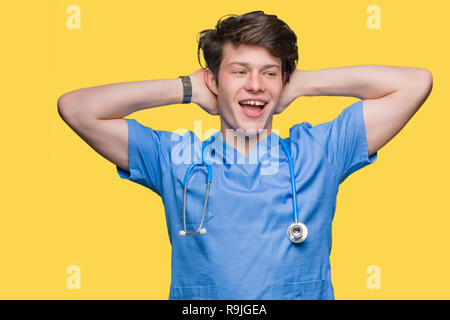 Giovane medico medico che indossano uniformi su sfondo isolato rilassante e stretching con le braccia e le mani dietro la testa ed il collo, sorridendo felice Foto Stock