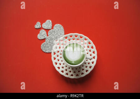 Fresco verde Matcha caffè con un modello cuore su uno sfondo rosso con molti cuori. Concetto per il giorno di San Valentino o il giorno della donna. Foto Stock
