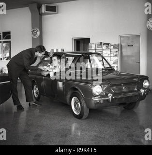 1965, storico, un uomo in cantante showroom auto seduti in un cantante (Hillman) Imp auto, England, Regno Unito essendo consegnato alcuni tasti di grandi dimensioni. Le 2 porte piccola economia auto è stata costruita dal gruppo Rootes per competere con BMC popolare 'Mini' e presentava diversi design innovativi elementi per il suo giorno, come un risparmio di spazio posteriore in alluminio-motore, con trazione posteriore. Il 'Singer' Imps badge sono stati progettati Hillmans intesi a leggermente più sistemazione di piccoli acquirenti di auto. Ma i problemi di affidabilità che tormenta la vettura e le sue perdite ha visto il britannico gruppo Rootes presi in consegna dall'americana Chrysler Corporation nel 1967. Foto Stock