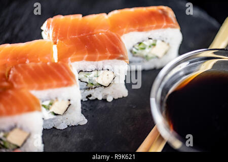 Macro shot di deliziosi piatti di riso sushi rotoli sulla pietra nera piastra con salsa di soia e bastoncini Foto Stock