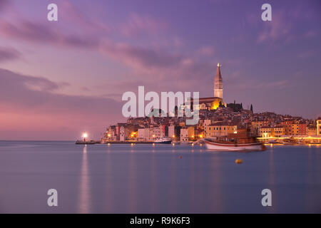 Vista della città di Rovigno in Croazia. Luce rosa tramonto con le luci della città in fase di accensione. Barche sfocate movimento dovuto alla lunga esposizione Foto Stock