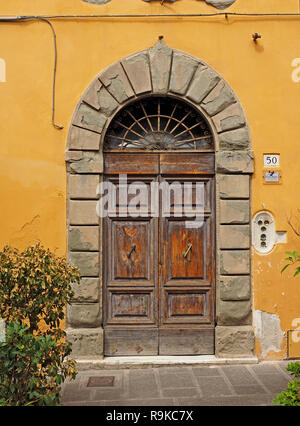 Imponente portale ad arco n. 50 con grandi indossato in legno porte doppie e ritaglio con griglia in metallo in tipica strada stretta a Pisa, Italia Foto Stock