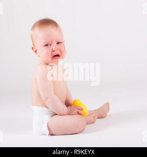 Bella nove mese Gridando bambino nel pannolino seduto a terra - studo shoot Foto Stock