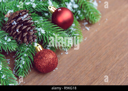 Sfondo di natale. Abete rami, rosso palla di Natale e pigne di neve decorazione su una tavola di legno. con copia spazio per il testo. Foto Stock