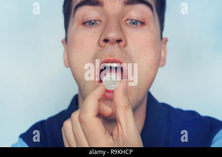 Giovane uomo mette in bocca una aspirazione di una pillola per il mal di gola. Auto-medicazione per influenza e freddo. Malati con un mal di gola, menta per un alito fresco. Foto Stock