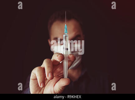 Fuori fuoco medico con una siringa in uno sfondo scuro. medico continua a parlare nelle mani di una siringa con un farmaco. Medico afosa. Lavoratori non qualificati specia Foto Stock