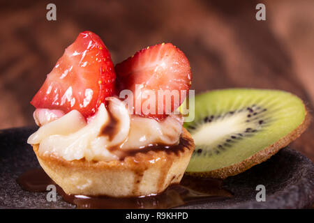 Frutta e bacche dessert crostata con kiwi e fragola su sfondo di legno. Fresh deliziosa torta dolce con fragole, kiwi e crema. Foto Stock