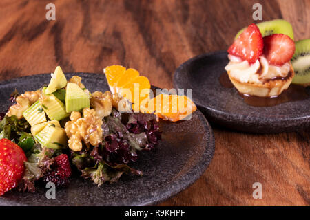 Insalata verde con frutta e bacche dessert crostata con kiwi e fragola con arance pigmentate Alligator Pear, barbabietole, semi e noci su una tavola di legno backgroun Foto Stock