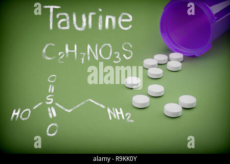 Pills fuoriuscita da un vaso aperto su sfondo verde, formulazione chimica di taurina scritto con un gessetto, immagine concettuale Foto Stock