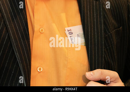 Poche banconote, dieci Lei rumeno sporgente dalla parte anteriore nella tasca della camicia di un imprenditore in un vestito. closeup vivida immagine Foto Stock