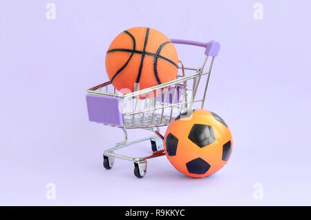 Orange basketball e calcio nel carrello su viola. Il concetto di vendita di attrezzature sportive, previsioni per eventi sportivi, scommesse sportive Foto Stock