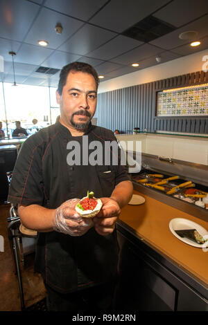 Utilizzando una varietà di ingredienti, un cuoco ispanica crea un rotolo di mano snack presso un ristorante giapponese in Costa Mesa, CA. Foto Stock