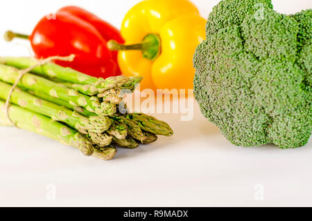 Asparagi, succosa rosso e arancio peperoni con una coda verde si trova accanto al fascio di lattuga e broccoli sono su sfondo bianco. isolato Foto Stock