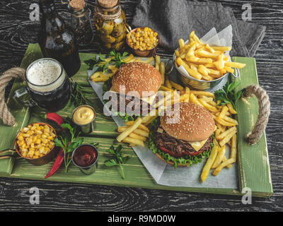 Barbeque tirato carni bovine sandwich, hamburger, patatine fritte, salsa, birra scura, mais su un vassoio in legno Foto Stock