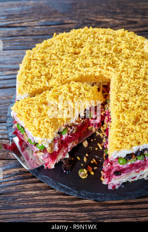 Sette deliziose torte a strati con insalata di verdure, uova sode, prugne, noci e carne di pollo su una piastra nera su un vecchio tavolo di legno, verticale Foto Stock