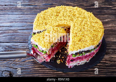 Sette deliziose torte a strati con insalata di verdure, uova sode, prugne, noci tritate e shredded carne di pollo su una piastra nera su un vecchio woo Foto Stock