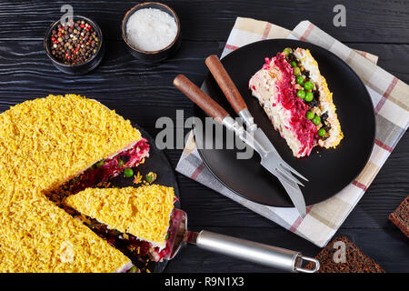 Sette deliziose torte a strati con insalata di verdure, uova sode, prugne, noci tritate e shredded carne di pollo su una piastra nera su un nero wo Foto Stock