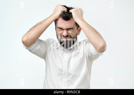 Enraged giovane impreditore tirando i suoi capelli fuori per esasperazione, avente un burnout sul lavoro Foto Stock