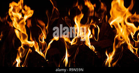 Un accogliente caminetto. Tronchetti di legno bruciando, sfondo scuro, relax e casa calda, primo piano con i dettagli Foto Stock