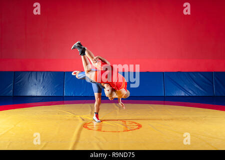 Il concetto di equo di wrestling. Due greco-romane lottatori in rosso e blu uniforme wrestling su sfondo di un giallo tappeto di wrestling in palestra Foto Stock