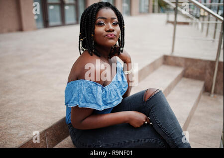 Attraente americano africano donna con i timori di indossare jeans seduti sulle scale. Foto Stock