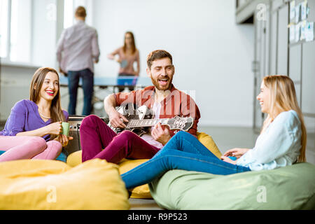 Un gruppo di giovani collaboratori divertirsi a suonare la chitarra e giocare a tennis da piccolo durante la pausa caffè in ufficio Foto Stock