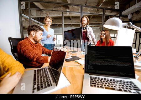 Un gruppo di giovani collaboratori vestito casualmente a lavorare insieme sul computer in ufficio moderno interno Foto Stock