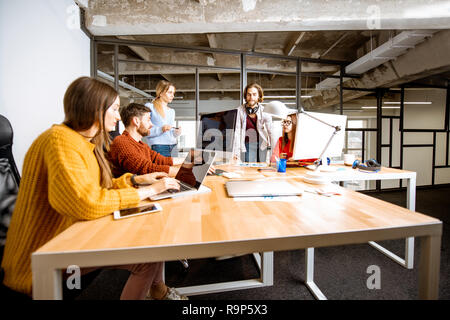 Un gruppo di giovani collaboratori vestito casualmente a lavorare insieme sul computer in ufficio moderno interno Foto Stock