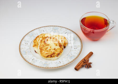 La cheesecake su un piattino con marmellata e tè. cottage cheese frittelle o pancake con confettura di fragole e una tazza di tè su un tavolo bianco. i tradizionali russi Foto Stock