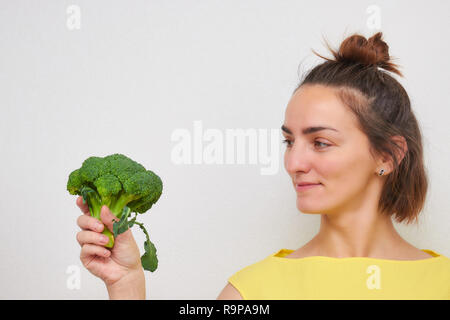 Allegro, bello, sottile, ragazza con broccoli infiorescenze nelle sue mani isolate su uno sfondo luminoso. donna di aspetto Europeo. Foto Stock