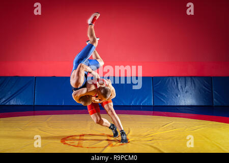 Il concetto di equo di wrestling. Due giovani uomini in blu e rosso collant di wrestling sono wrestlng e facendo un suplex wrestling su un giallo tappeto di wrestling Foto Stock