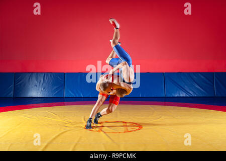 Il concetto di equo di wrestling. Due giovani uomini in blu e rosso collant di wrestling sono wrestlng e facendo un suplex wrestling su un giallo tappeto di wrestling Foto Stock