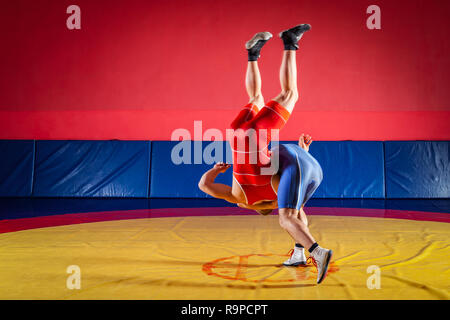 Due giovani uomini in blu e rosso collant di wrestling sono wrestlng e facendo un suplex wrestling su un giallo tappeto di wrestling in palestra. Il concetto di equo Foto Stock