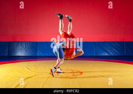 Due giovani uomini in blu e rosso collant di wrestling sono wrestlng e facendo un suplex wrestling su un giallo tappeto di wrestling in palestra. Il concetto di equo Foto Stock