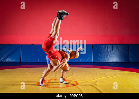 Due giovani uomini in blu e rosso collant di wrestling sono wrestlng e facendo un suplex wrestling su un giallo tappeto di wrestling in palestra. Il concetto di equo Foto Stock