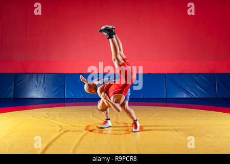 Due giovani uomini in blu e rosso collant di wrestling sono wrestlng e facendo un suplex wrestling su un giallo tappeto di wrestling in palestra. Il concetto di equo Foto Stock