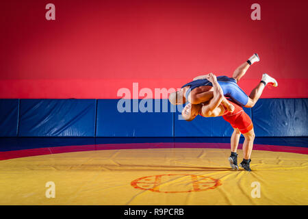 Due giovani uomini in blu e rosso collant di wrestling sono wrestlng e facendo un suplex wrestling su un giallo tappeto di wrestling in palestra. Il concetto di equo Foto Stock