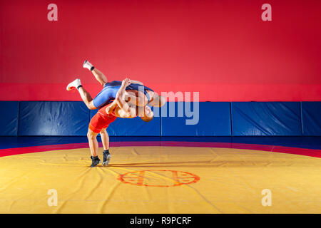 Due giovani uomini in blu e rosso collant di wrestling sono wrestlng e facendo un suplex wrestling su un giallo tappeto di wrestling in palestra. Il concetto di equo Foto Stock