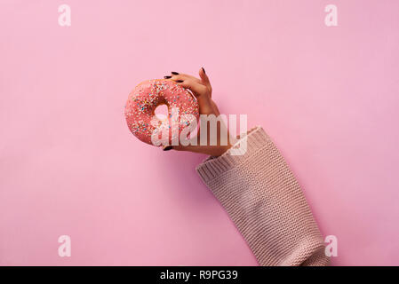 Femmina di mano azienda ciambella su sfondo rosa. Vista superiore, piatto laici. Dolce, dessert, il concetto di dieta. Banner con copia spazio. Perdita di peso dopo le vacanze. Foto Stock