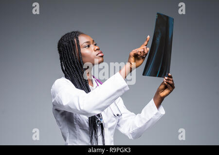 Closeup ritratto di donna medico personale sanitario con il bianco labcoat, guardando a corpo pieno x-ray immagine radiografica, scansione CT, MRI, isolato grigio b Foto Stock