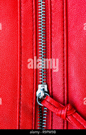 Zipper parzialmente open close up dettaglio foto macro su una pelle rossa sullo sfondo di texture in formato verticale. Foto Stock