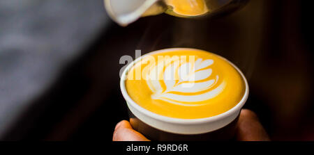 Caffè africani Barista versando una foglia forma con schiuma di latte in un take away cup Foto Stock