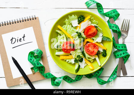 Alimentazione sana Dieta e concetto. Piastra di colore verde con verdure fresche insalate e misurazione su un tavolo di legno. Foto Stock