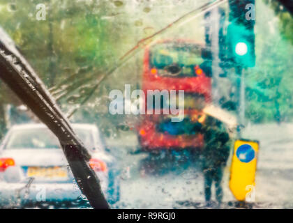 London street scene sottratto dalla pioggia su di un parabrezza di automobile in un giorno di pioggia. Un bus rosso può essere visto e un uomo con il cartone sopra la sua testa per shelte Foto Stock