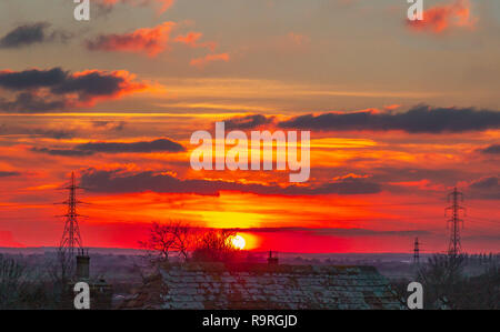 Tramonto su una sera Nuvoloso sui tetti e mostrando tralicci e linee di alimentazione stagliano su entrambi i lati del tramonto Foto Stock