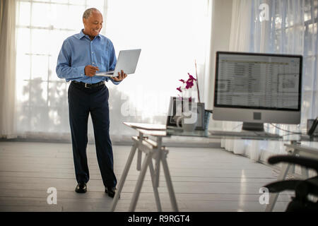 Allegro imprenditore maturo lavora sul suo computer portatile nel suo ufficio di casa. Foto Stock