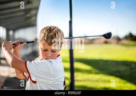 Giovane ragazzo in oscillazione un golf club presso un driving range. Foto Stock