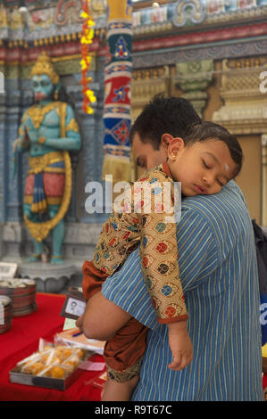 Un etnica indiana bambino che dorme sul suo padre lo spallamento nella parte anteriore dello Sri Krishnan (Hindu) Tempio, Waterloo San, Singapore, a Hanuman statua in b/g Foto Stock