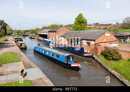 Braunston, Northants. Elevato punto di vista di un blu narrowboat vela su un canale. Le imbarcazioni vengono ormeggiate su entrambi i lati. Un cane è di camminare sulla strada alzaia. Foto Stock