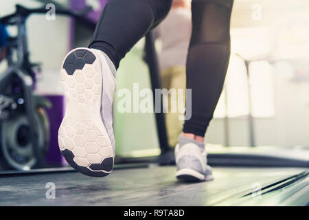 Ragazza Fitness in esecuzione sul tapis roulant. Donna con gambe muscolare nella moderna palestra. una ragazza in bianco sneakers in esecuzione su un tapis roulant in palestra. Foto Stock